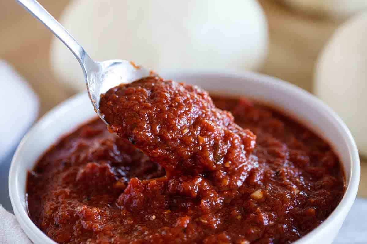 Making homemade pizza? You’ll want this Pizza Sauce Recipe! You only need 20 minutes and you’ll have a pizza sauce that will totally upgrade your homemade pizza! Bowl with pizza sauce recipe with a spoon.