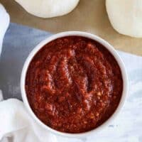 Bowl filled with pizza sauce with balls of pizza dough surrounding it.