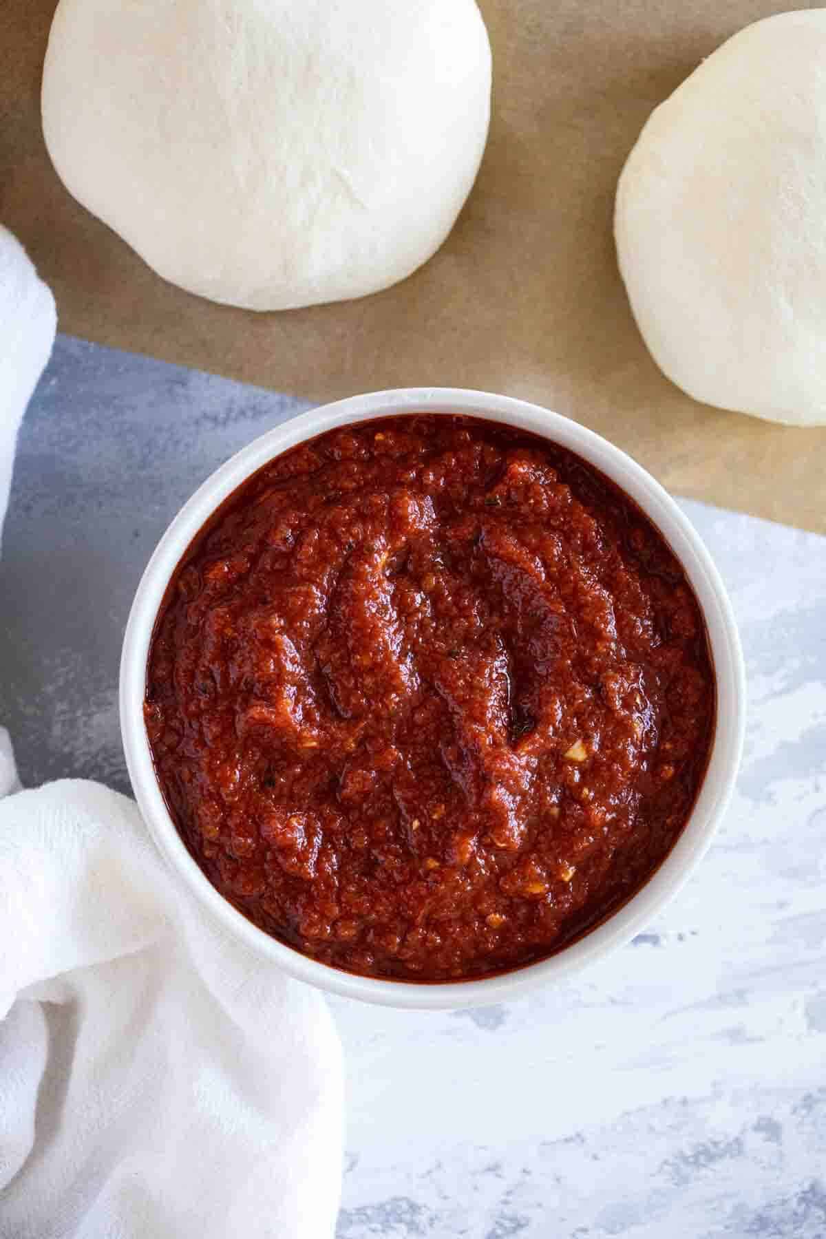 Bowl filled with pizza sauce with balls of pizza dough surrounding it.