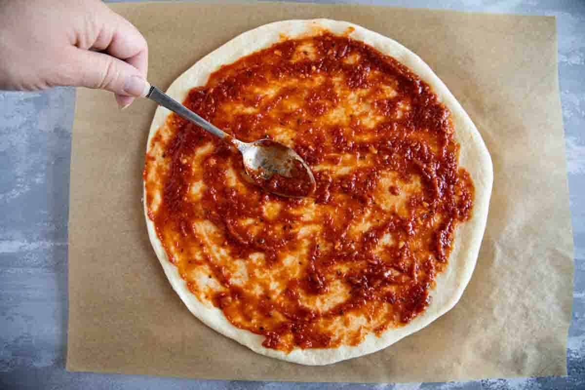 Spreading pizza sauce on pizza crust.