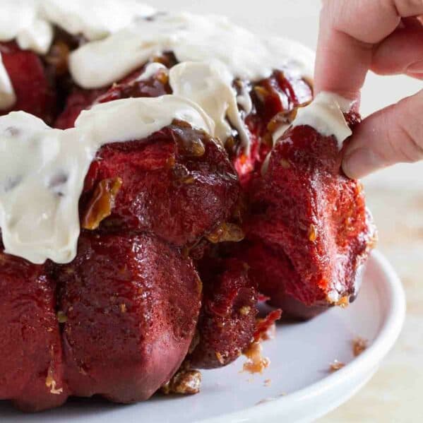 Fingers pulling a piece of red velvet pull apart bread from the loaf.