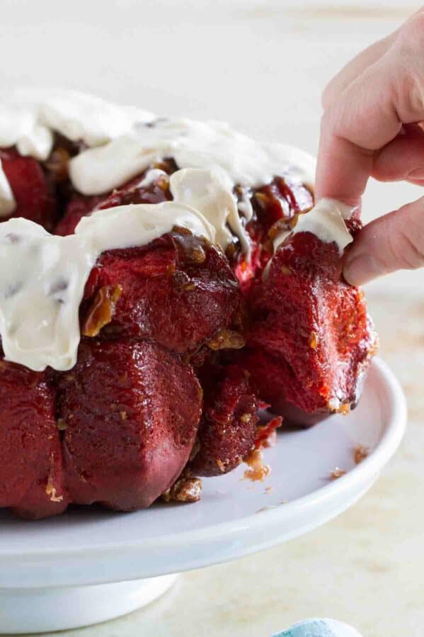 Fingers pulling a piece of red velvet pull apart bread from the loaf.