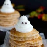 Stack of spiced ghost pancakes with a whipped cream ghost on top.