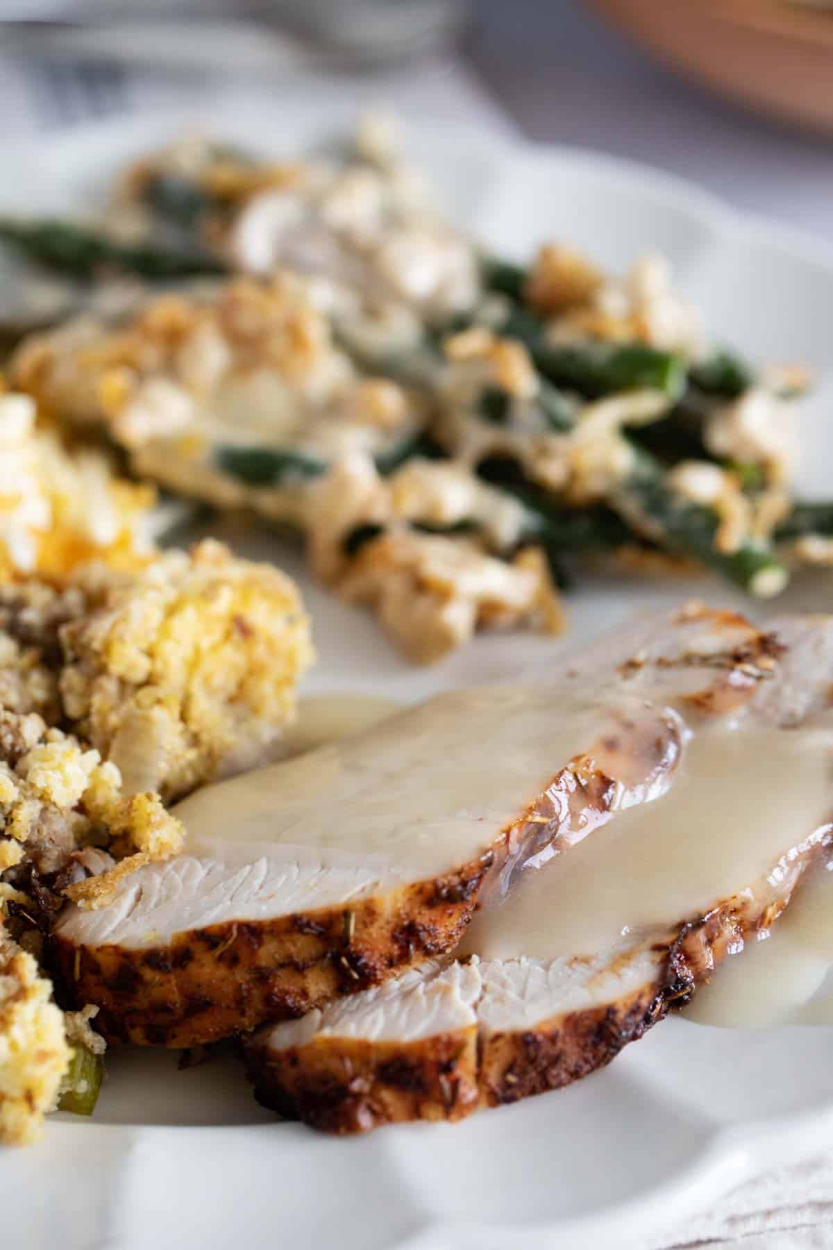 Slices of air fryer turkey breast with gravy on a plate with side dishes.