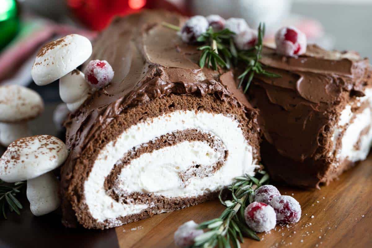 Bûche de Noël (Yule Log Cake) decorated with cranberries, rosemary, and meringue mushrooms.