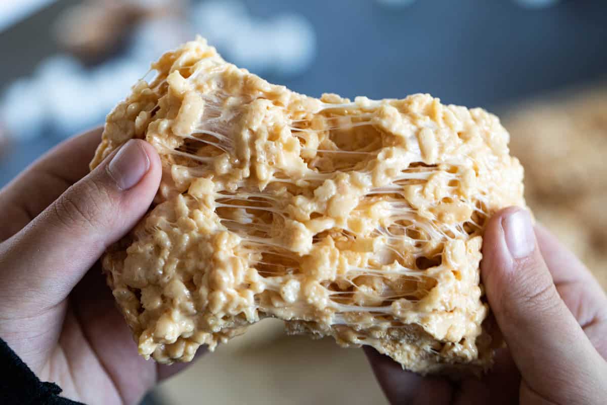 Hands pulling a caramel rice krispie treat apart.