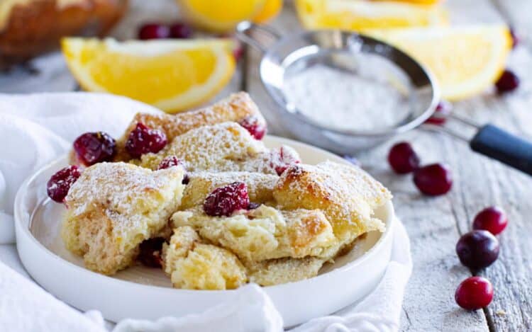 Small plate with a serving of cranberry orange baked French toast casserole sprinkled with powdered sugar.