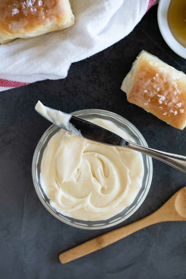 Bowl of honey butter with fresh rolls beside it.