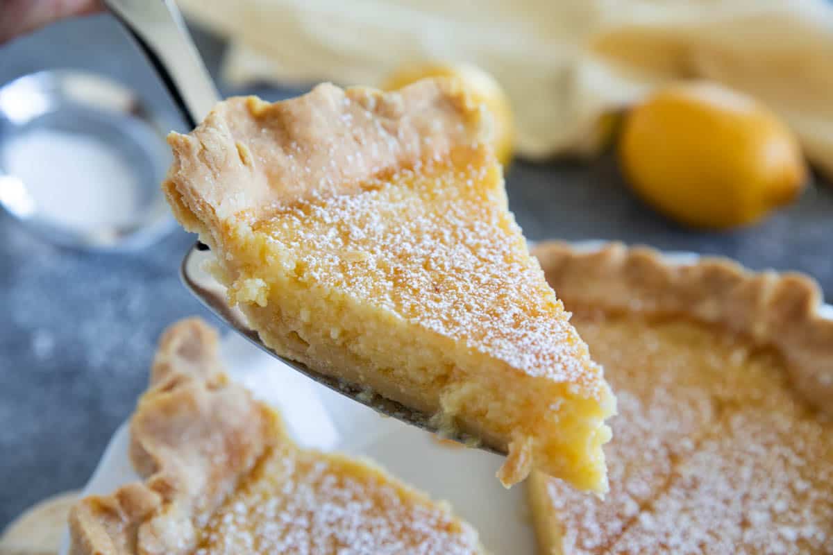 Removing a slice of lemon chess pie from a full pie.