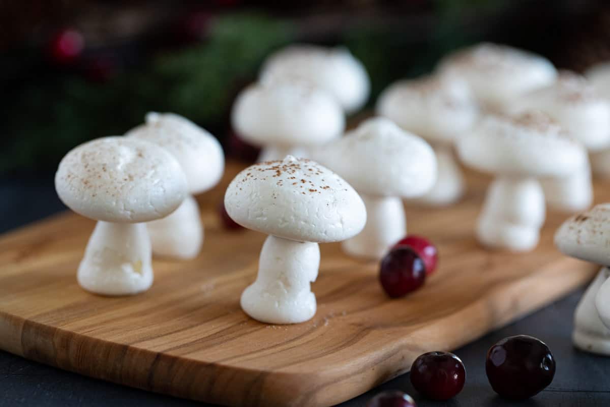 Meringue mushrooms on a cutting board with fresh cranberries.