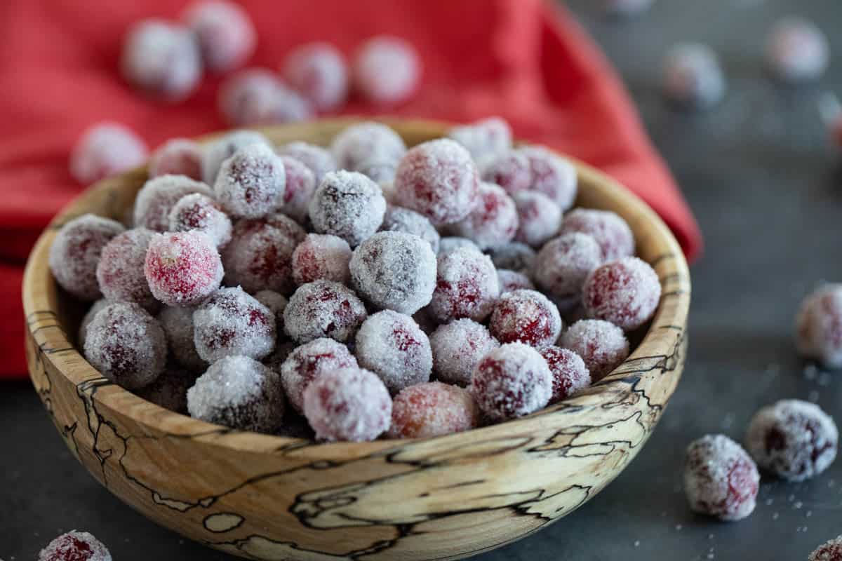 Sugared cranberries in a wooden bowl with some cranberries falling out.