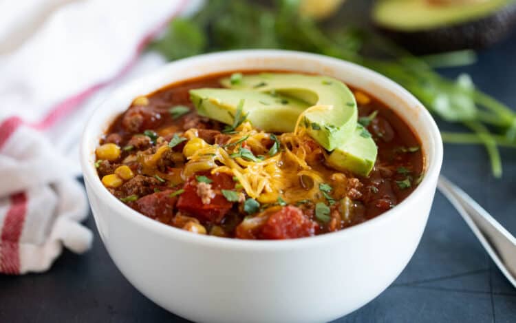 Bowl of taco soup topped with cheese and avocados.