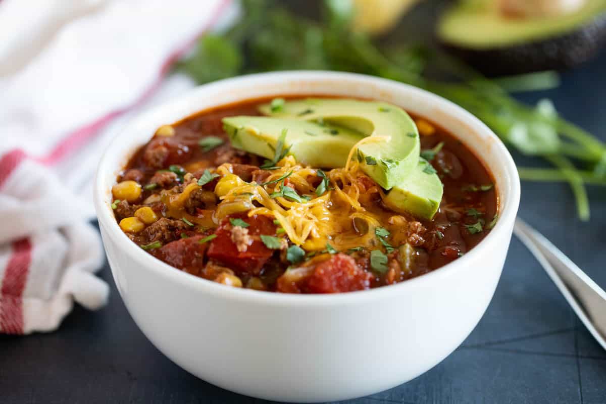 Bowl of taco soup topped with cheese and avocados.