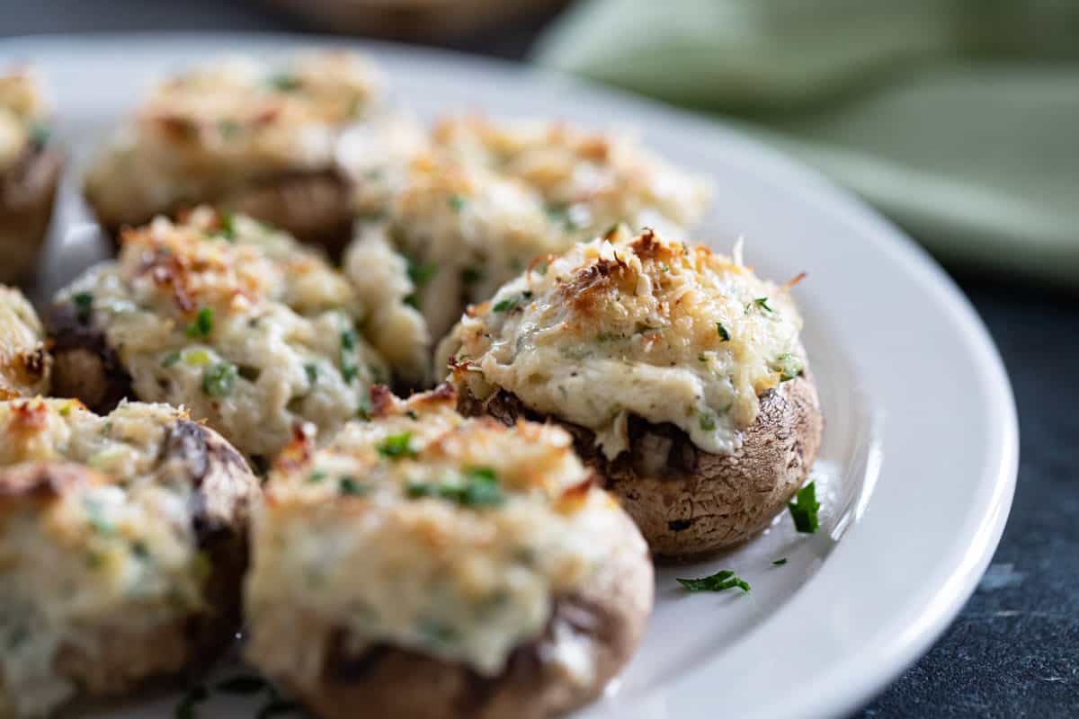 Crab Stuffed Mushrooms with toasted cheese and parsley on a white plate.
