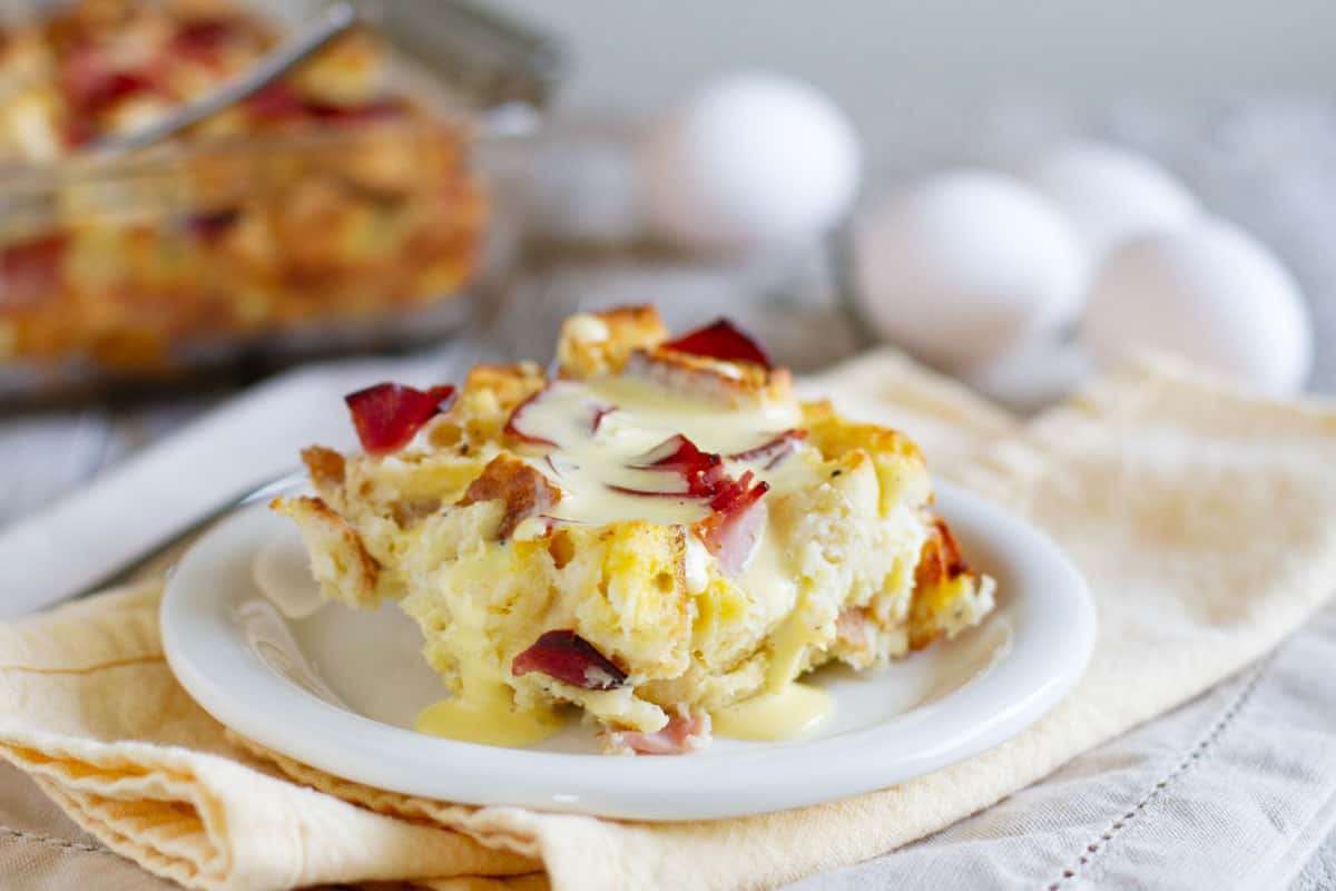 Eggs benedict made easy!! An Eggs Benedict Casserole is an overnight casserole with the flavors of eggs benedict that is served with an easy blender hollandaise sauce poured over the top. Piece of eggs benedict casserole on a plate, topped with homemade hollandaise sauce.