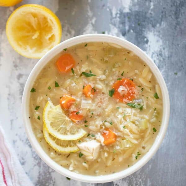 Bowl of Lemon Chicken Orzo Soup topped with lemon slices and parmesan cheese.