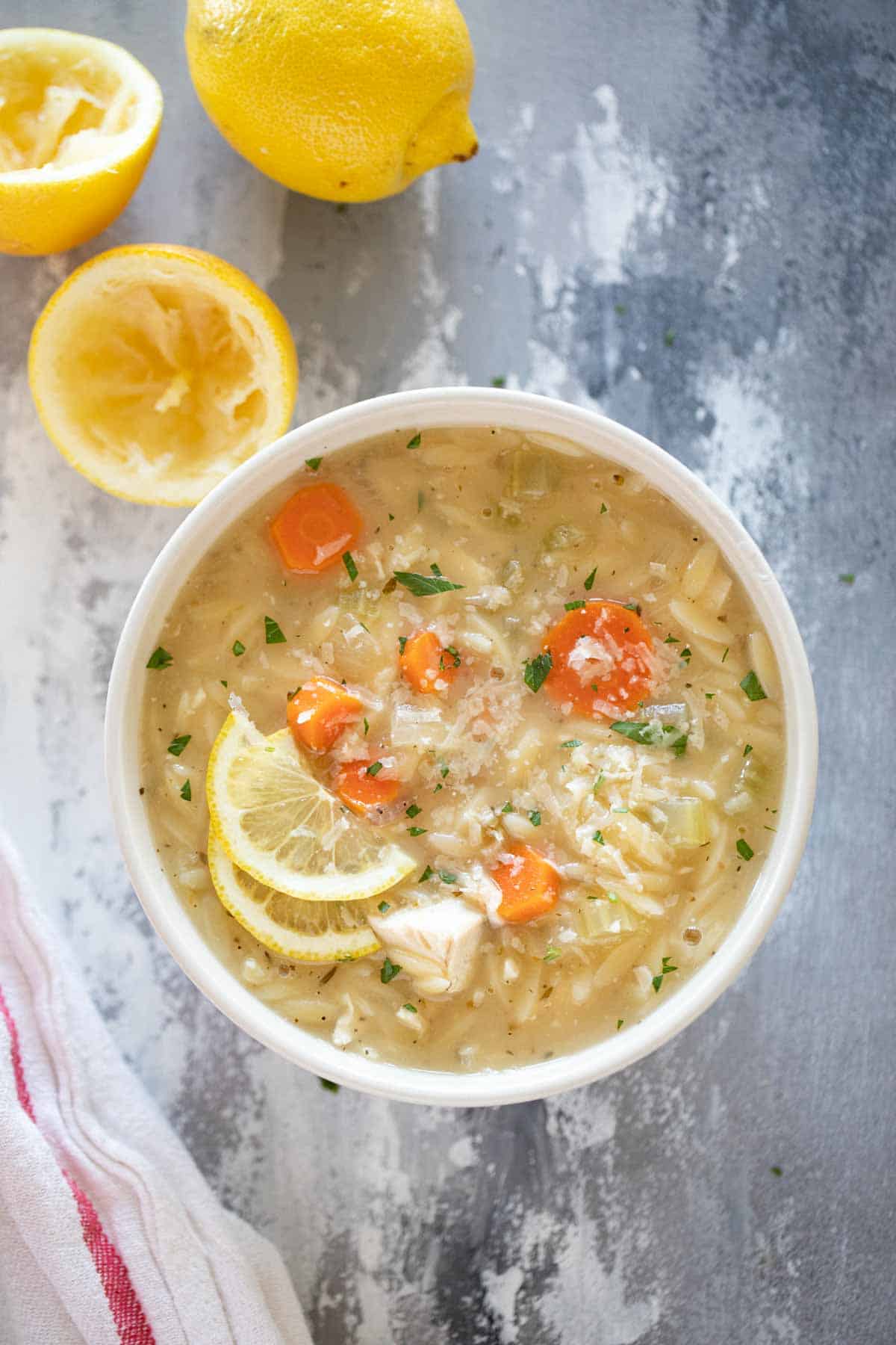Bowl of Lemon Chicken Orzo Soup topped with lemon slices and parmesan cheese.