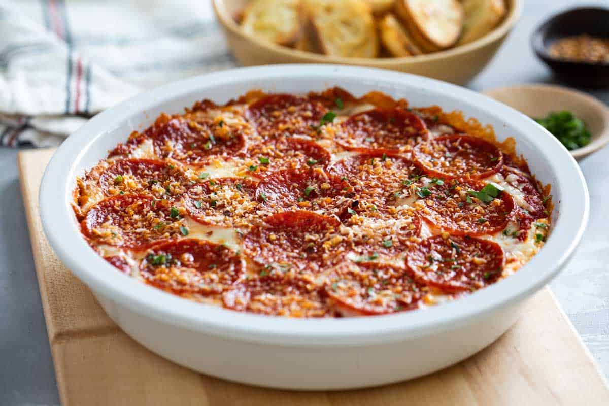 Pepperoni Pizza Dip in a white dish with baguettes behind.