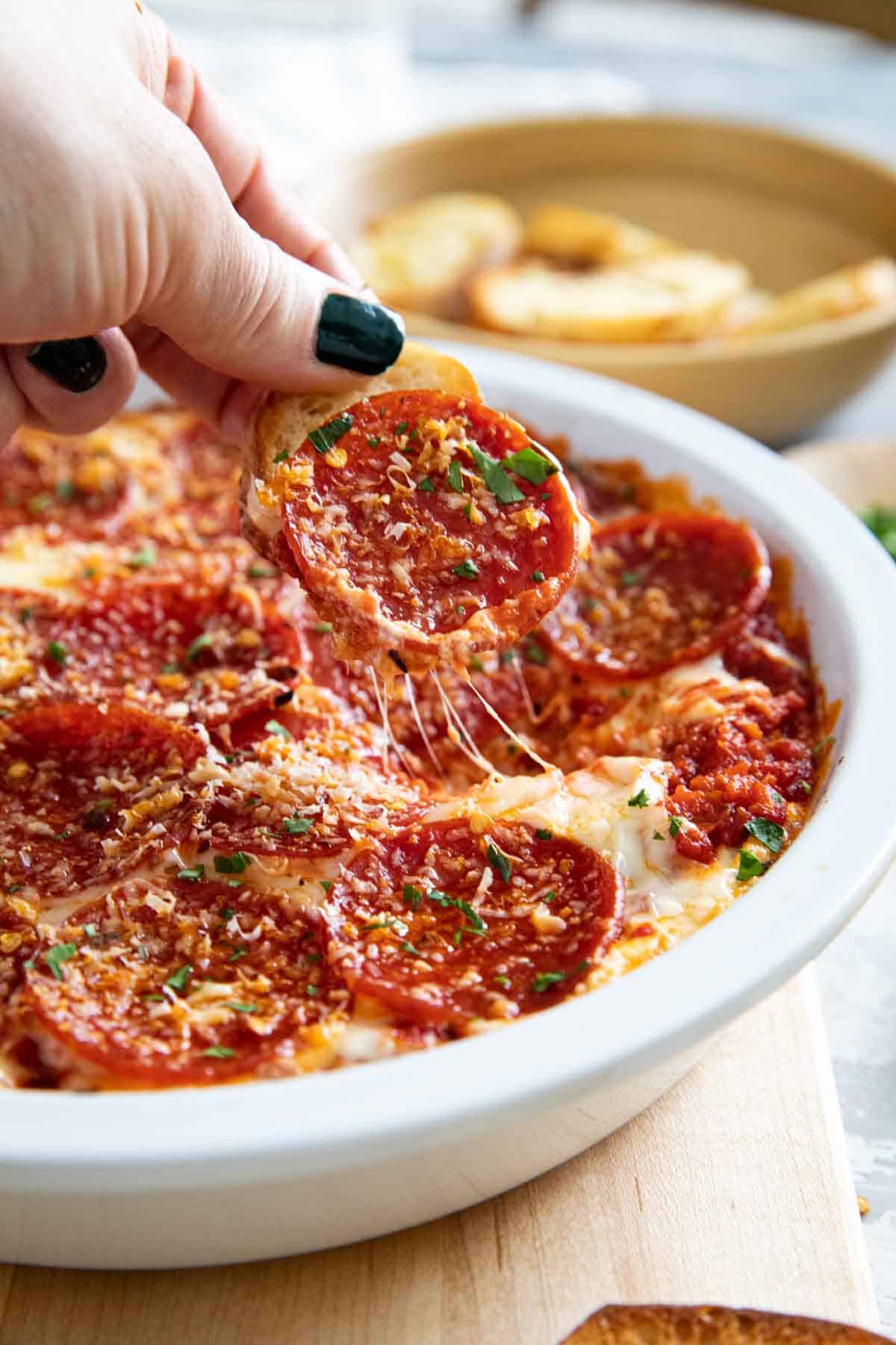 Pepperoni Pizza Dip in a pie dish with a baguette taking some out.