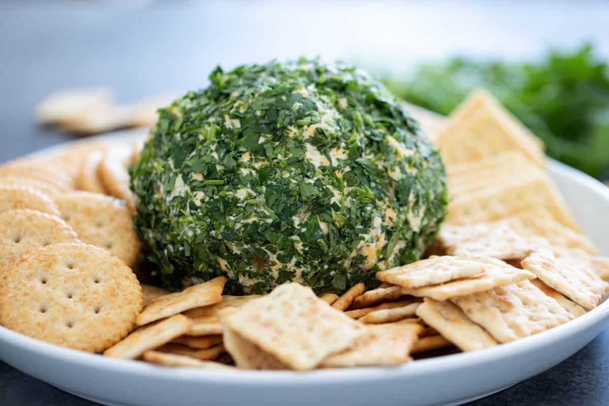 This Southwest Cheese Ball is filled with all of your favorite Tex-Mex flavors - green chiles, cheese, and cilantro. Great for parties or game nights. Southwest Cheese Ball covered in cilantro on a plate with various crackers.