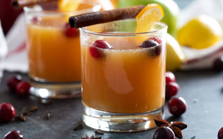 Glasses of hot wassail topped with cinnamon sticks and cranberries.