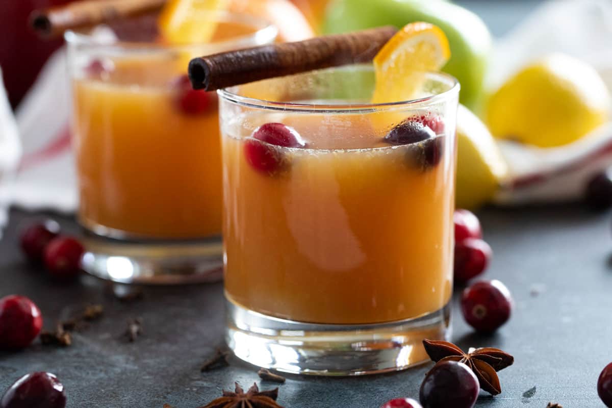 Glasses of hot wassail topped with cinnamon sticks and cranberries.