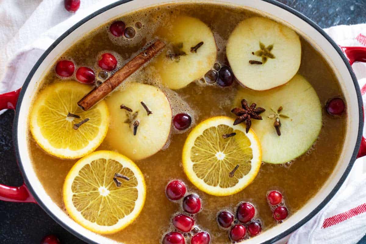 Pot filled with hot wassail topped with fruit slices, spices, and cranberries.