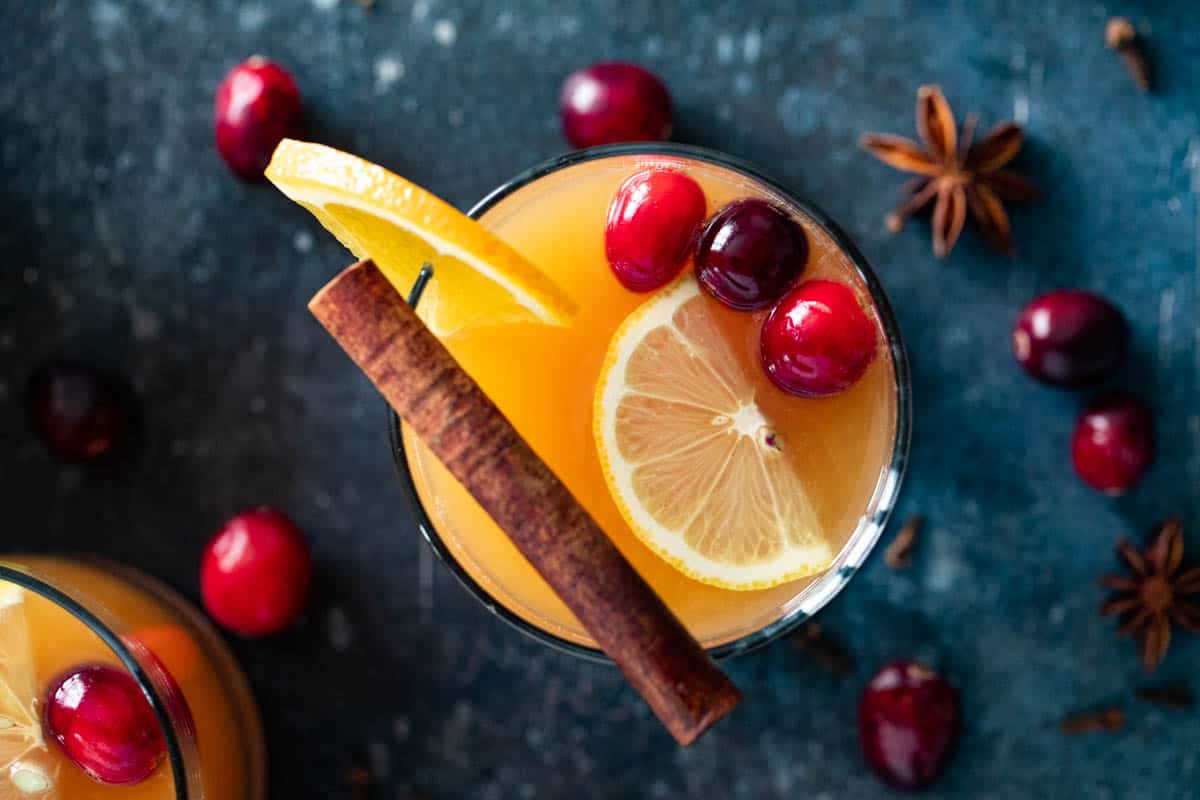 Glass filled with Wassail and topped with a cinnamon stick and cranberries.