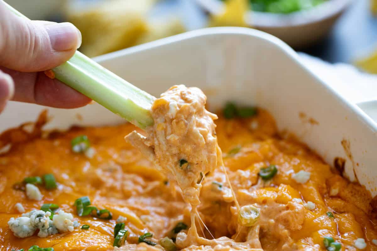 A classic game day appetizer, this Buffalo Chicken Dip is so popular for a reason! Filled with all of your favorite buffalo chicken flavors, this dip is super easy to make and always disappears. Dipping a celery stick into buffalo chicken dip.