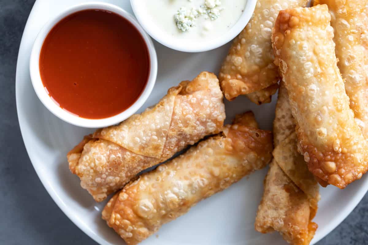 Plate with buffalo chicken egg rolls with dipping sauces.
