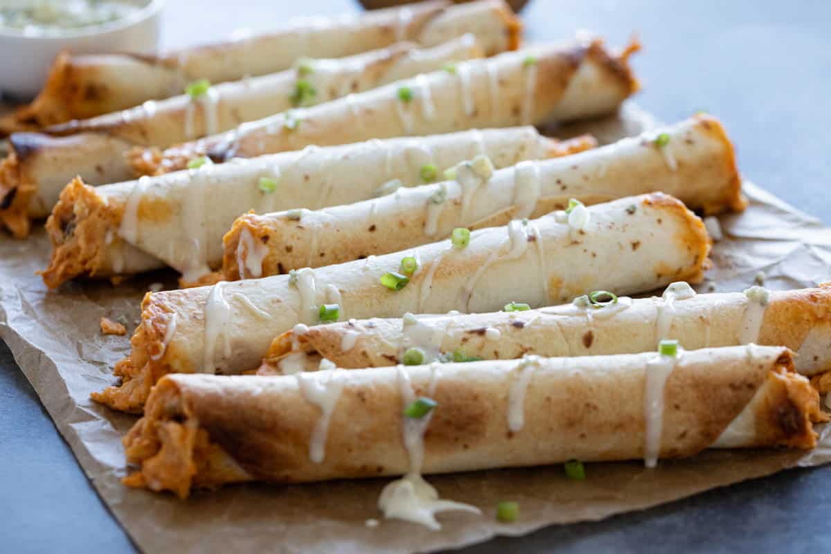 Buffalo Chicken Taquitos drizzled with blue cheese dressing on parchment paper.