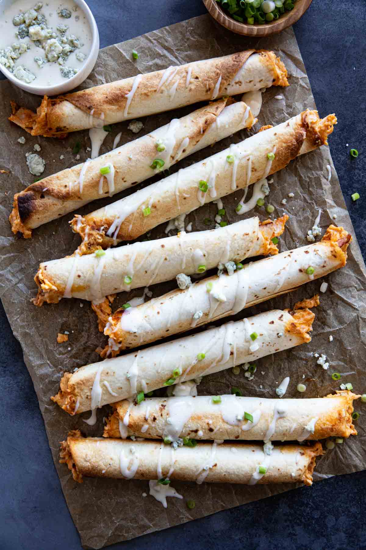 Buffalo Chicken Taquitos drizzled with blue cheese dressing and sliced green onions.