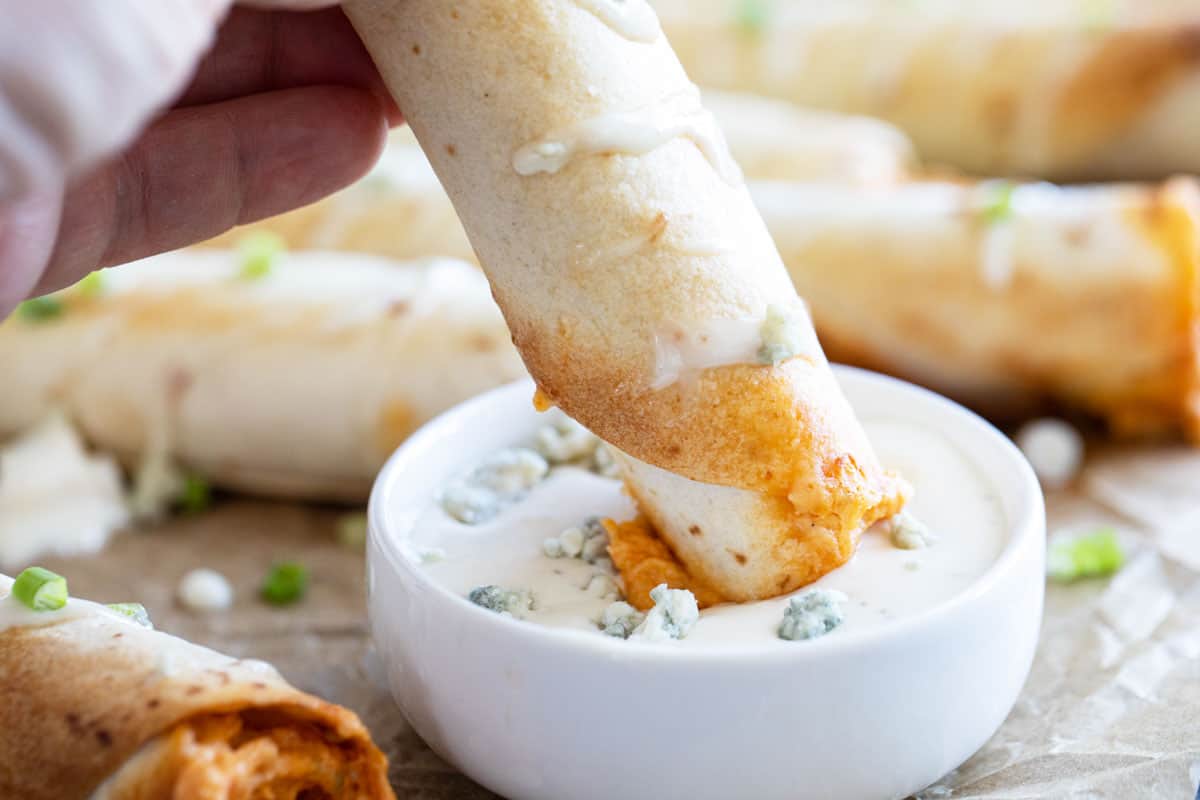 Perfect for the big game, or for a Friday night, any buffalo chicken lover will love these Buffalo Chicken Taquitos! Dipping a buffalo chicken taquito into blue cheese dressing.
