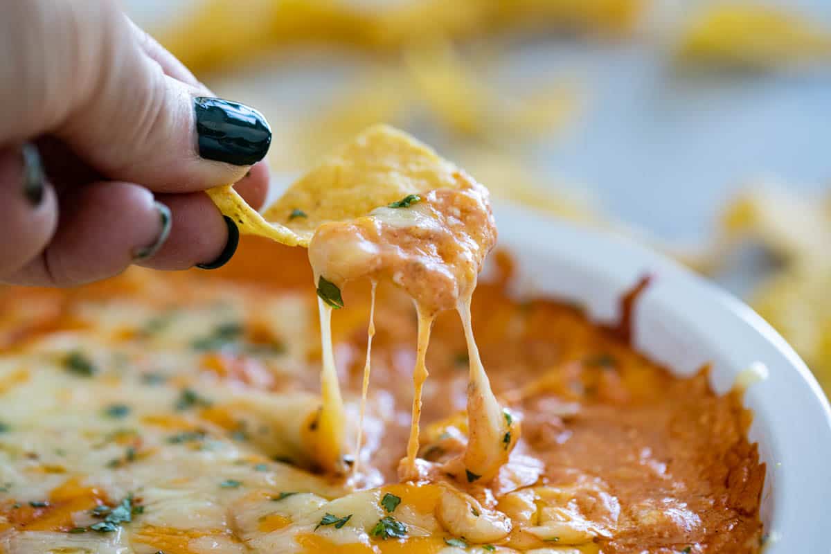 This easy, hot, Cheesy Mexican Dip is perfect for any group gathering. It only takes minutes to pull together before baking it off until hot and bubbly. Chip with Cheesy Mexican Dip topped with melted cheese.
