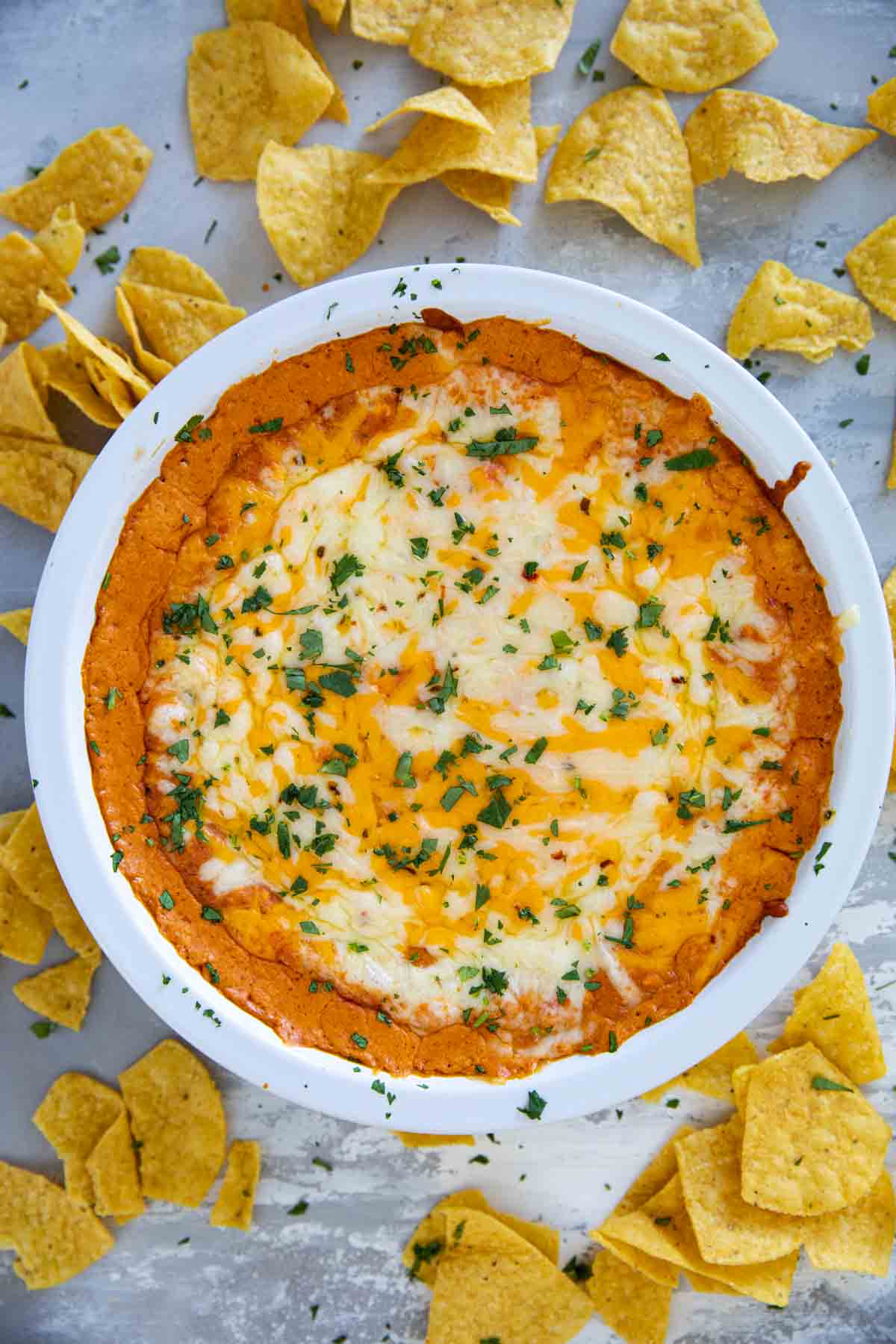 White pie dish filled with Cheesy Mexican Dip and surrounded by tortilla chips.