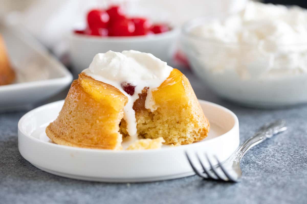 Pineapple upside down cupcake topped with whipped cream with a bite taken from it.