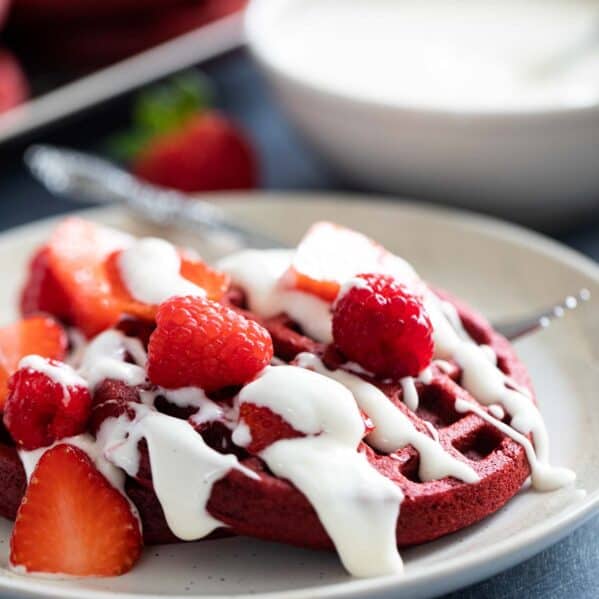 Red velvet waffles topped with a cream cheese drizzle, strawberries, and raspberries.