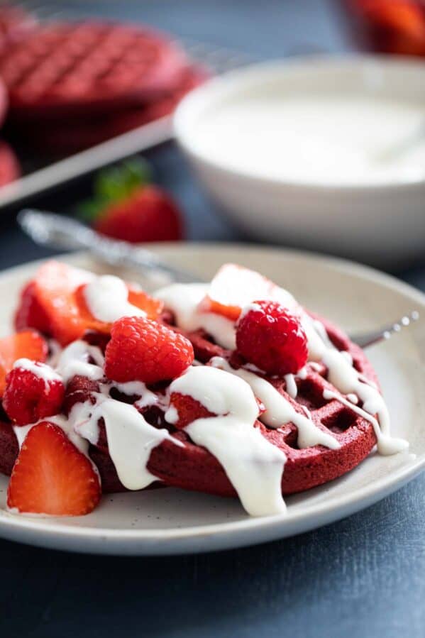 Red velvet waffles topped with a cream cheese drizzle, strawberries, and raspberries.