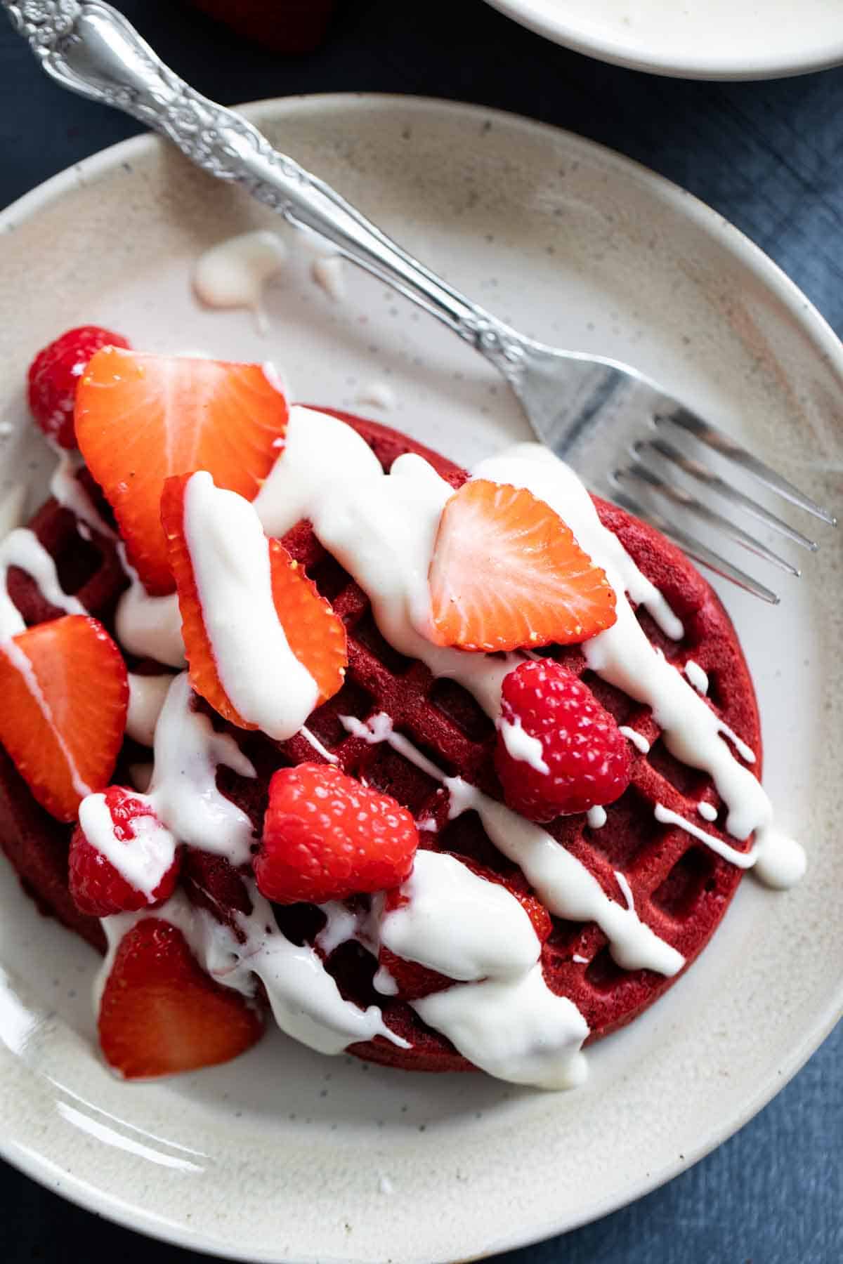 Red velvet waffles topped with berries and a cream cheese drizzle.