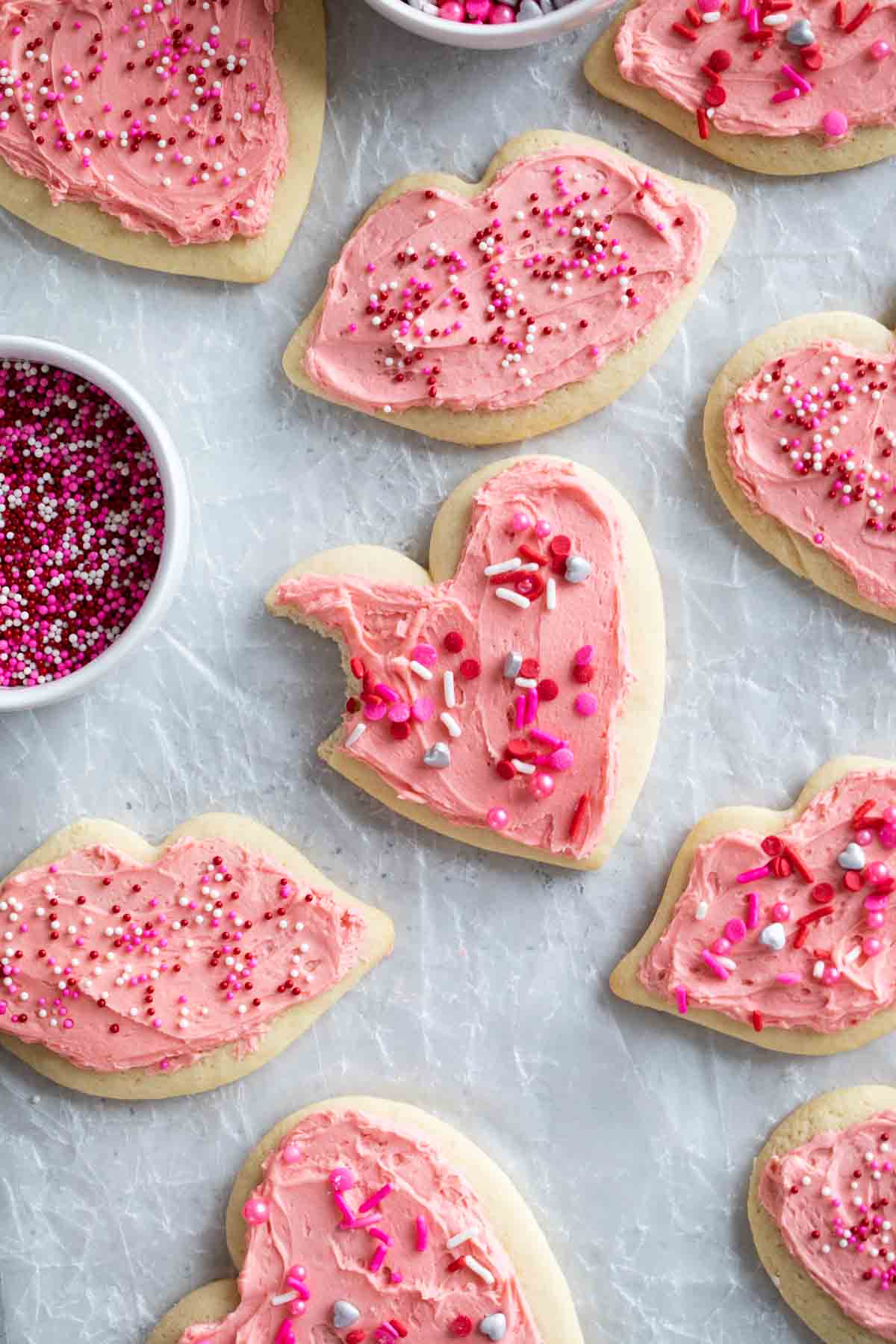 Valentine's Day Sugar Cookies on parchment with a bite taken from one cookie.