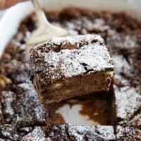 Scooping chocolate bread pudding from a baking dish.