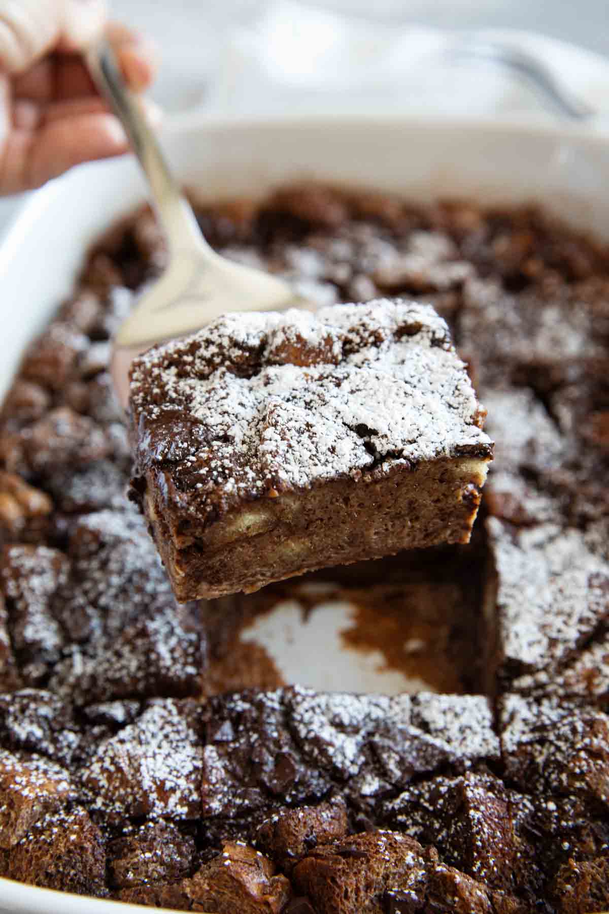 Scooping chocolate bread pudding from a baking dish.