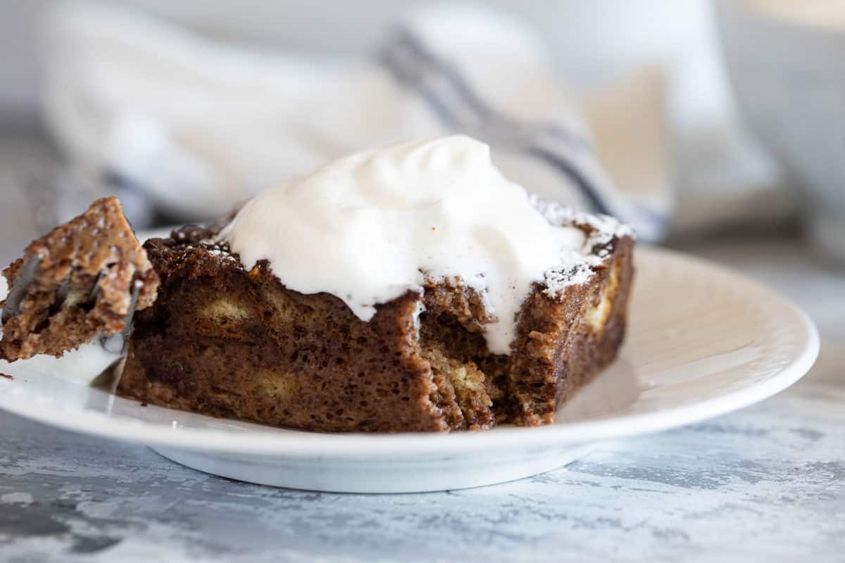 Piece of chocolate bread pudding topped with whipped cream with a bite taken from it.