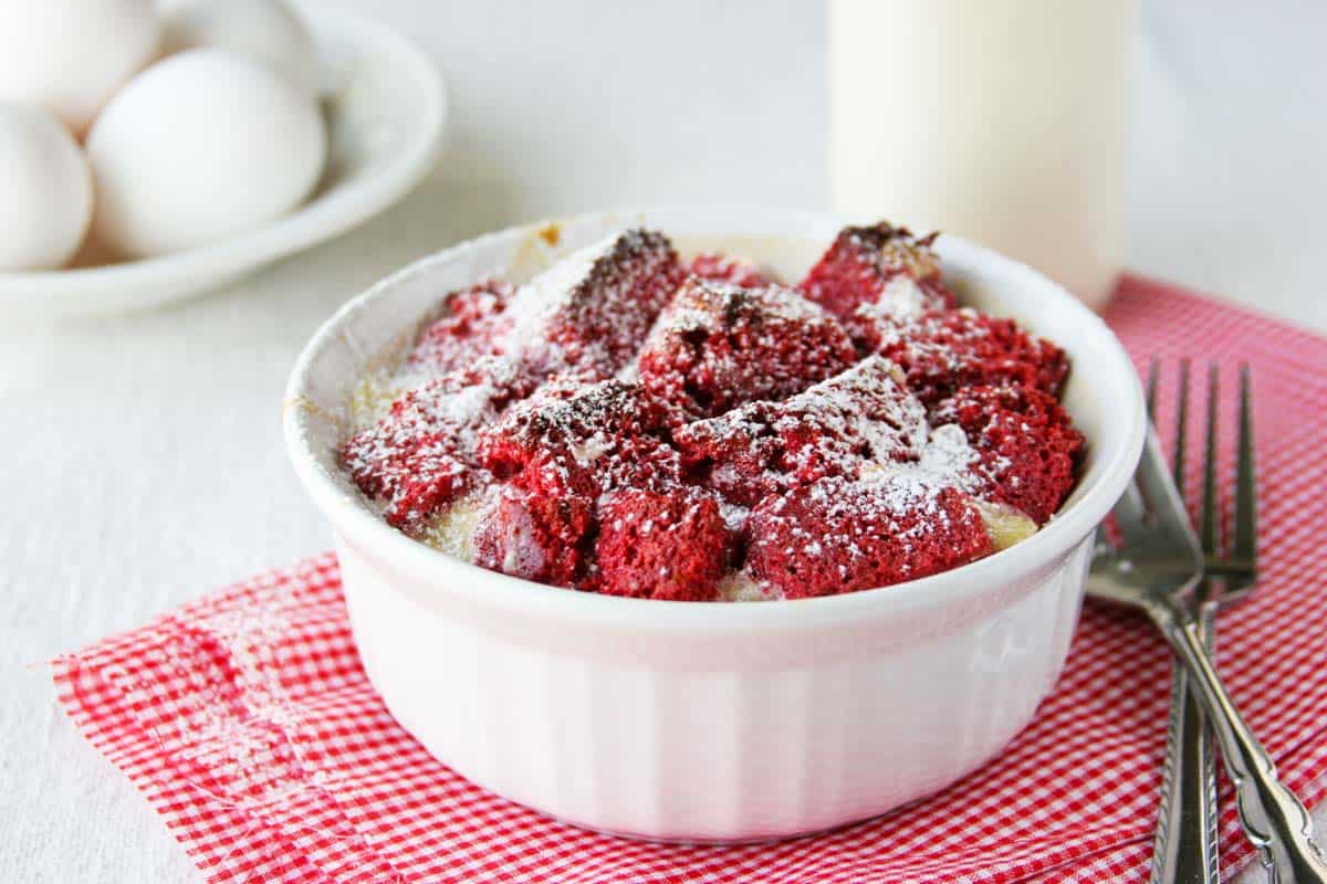 Want to impress your dinner guests? This red velvet bread pudding is not only stunning to look at, but it’s pretty darn tasty as well! Serving of red velvet bread pudding in a white ramekin.