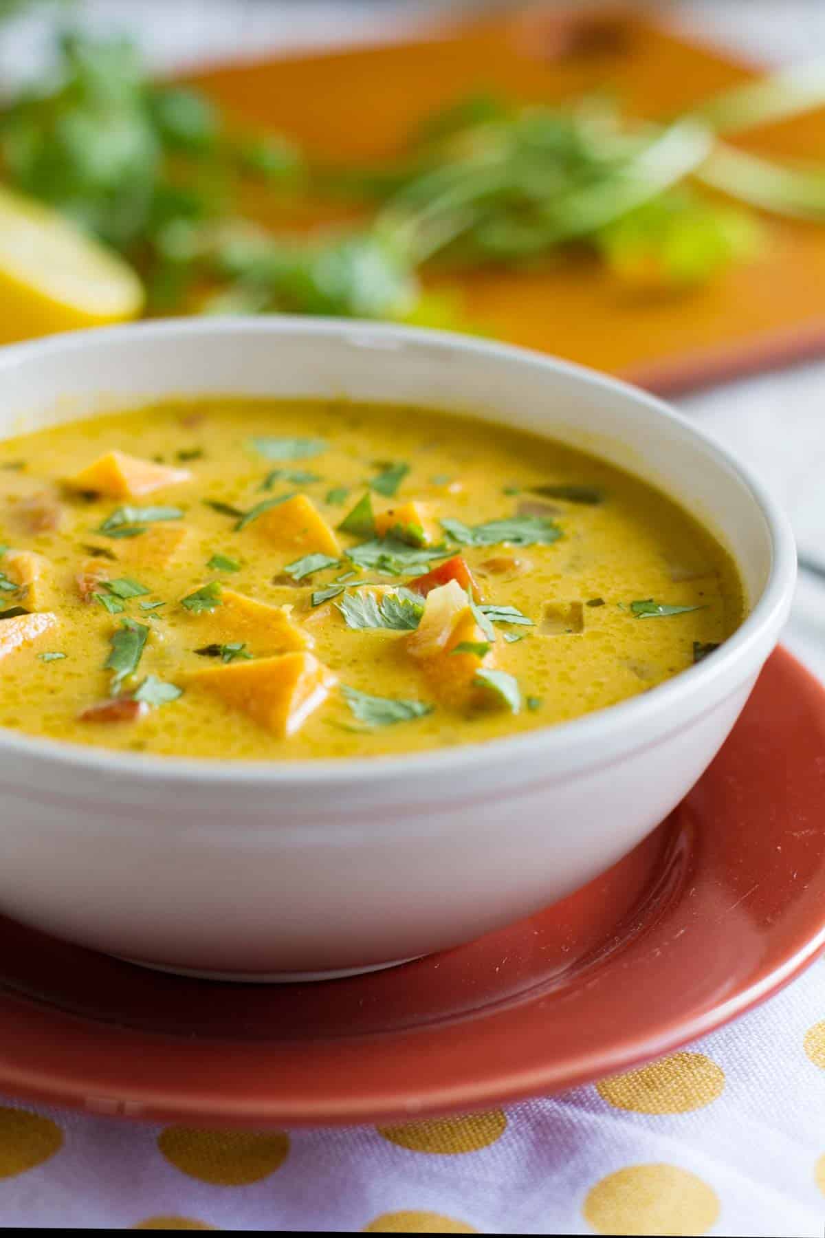 Bowl of roasted red pepper with sweet potato soup with ingredients in the background.