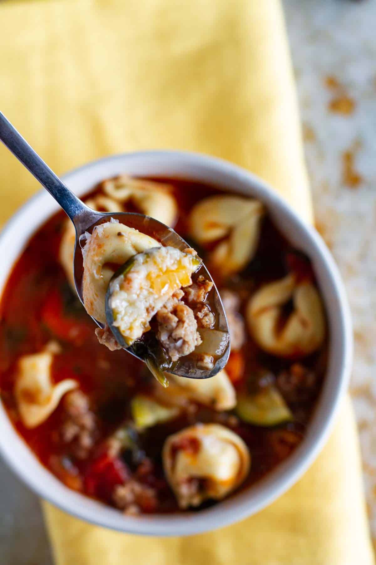 Spoonful of Sausage Tortellini Soup over a soup bowl.