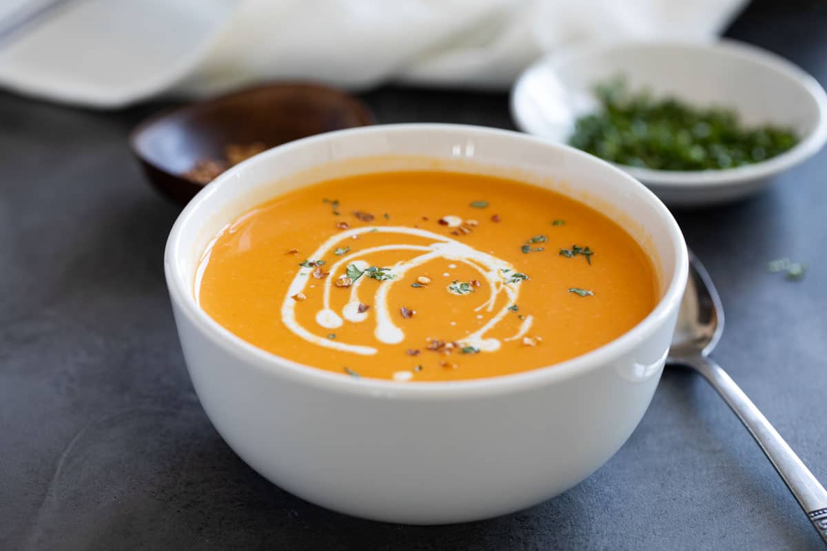 Bowl of sweet potato soup topped with red pepper flakes, cream, and parsley.