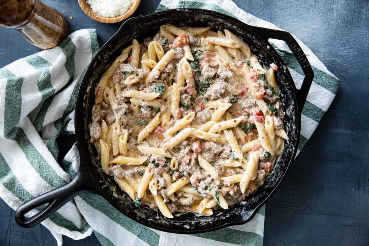 Cast iron skillet filled with Tuscan Pasta with Sausage, tomatoes, and spinach.