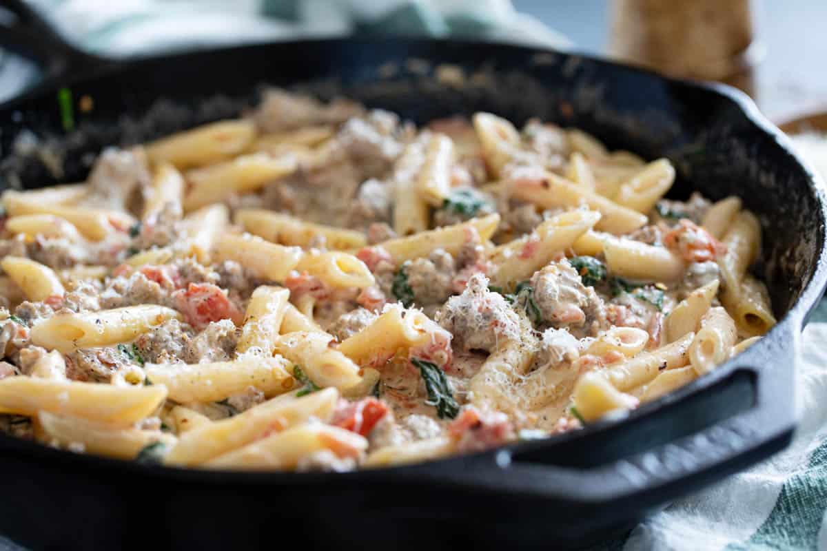 Skillet filled with Tuscan pasta with sausage topped with parmesan cheese.