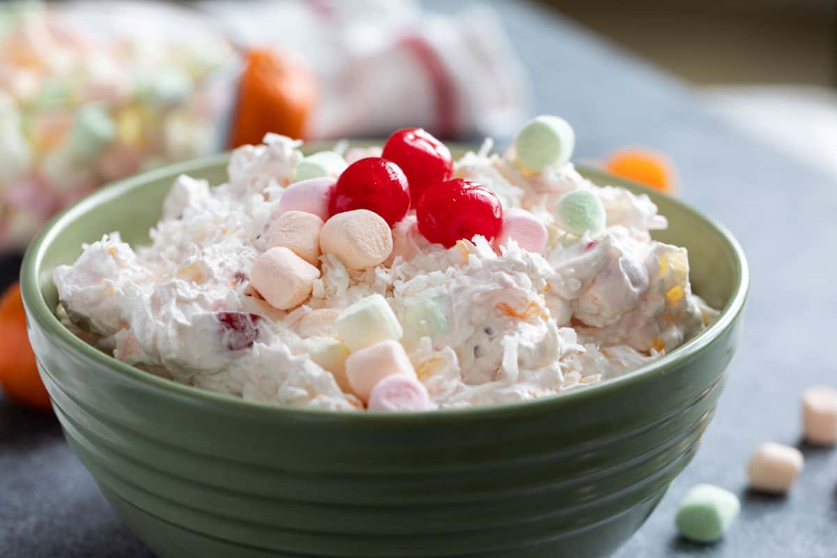 Bowl of Ambrosia Salad topped with marshmallows, cherries, and coconut.